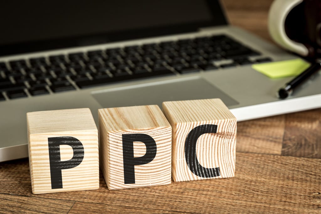 PPC (Pay Per Click) written on a wooden cube in front of a laptop